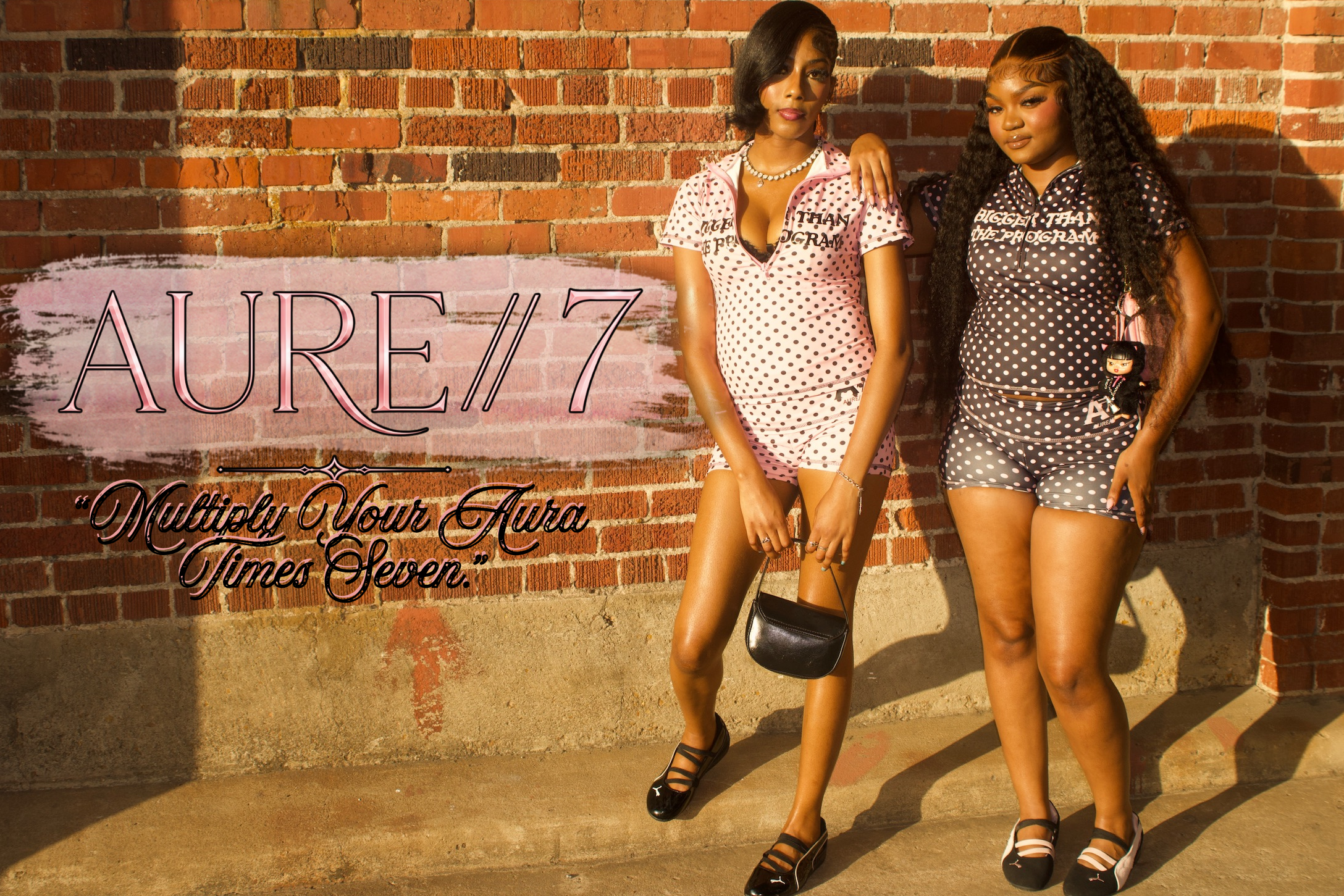 Two women posing against a brick wall with 'AURE 7' branding.